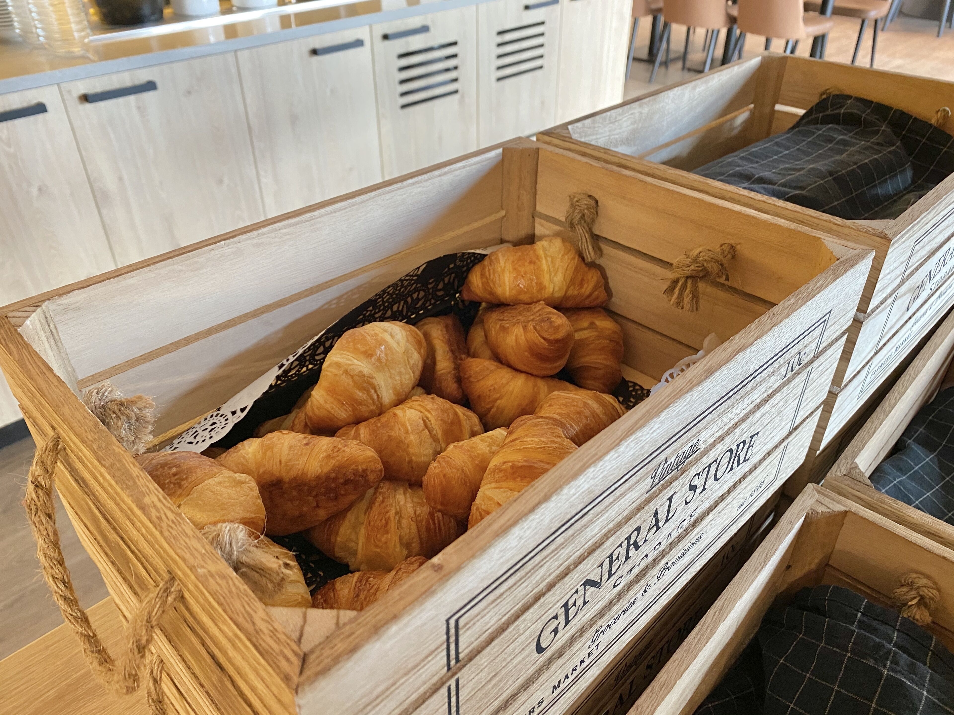 A wooden crate filled with croissants, labeled 'GENERAL STORE'.