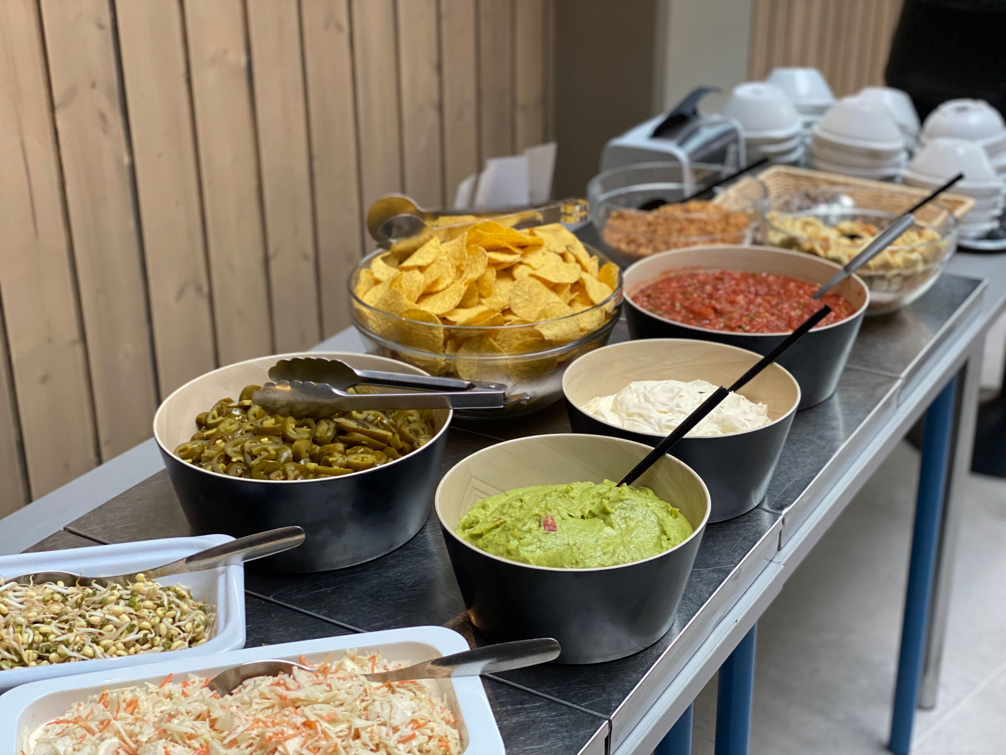 Ett buffébord med olika sorters mat, inklusive chips, salsa, guacamole, bönor och coleslaw.