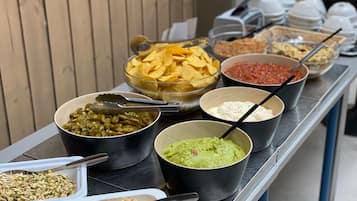 Ett buffébord med olika sorters mat, inklusive chips, salsa, guacamole, bönor och coleslaw.