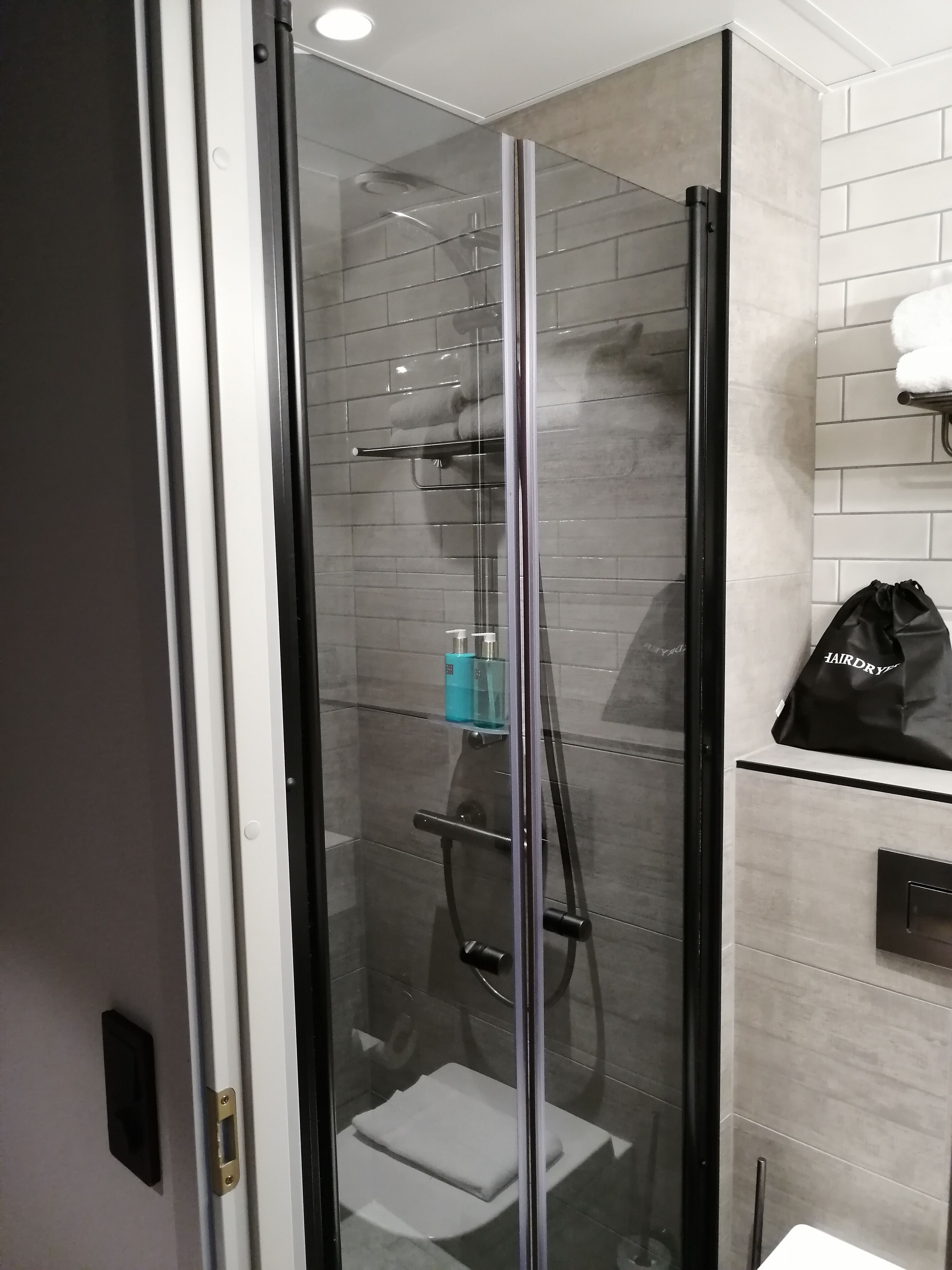 Un baño moderno con ducha de vidrio, un perchero y una bolsa con la etiqueta "HAIRDRY" en la pared.