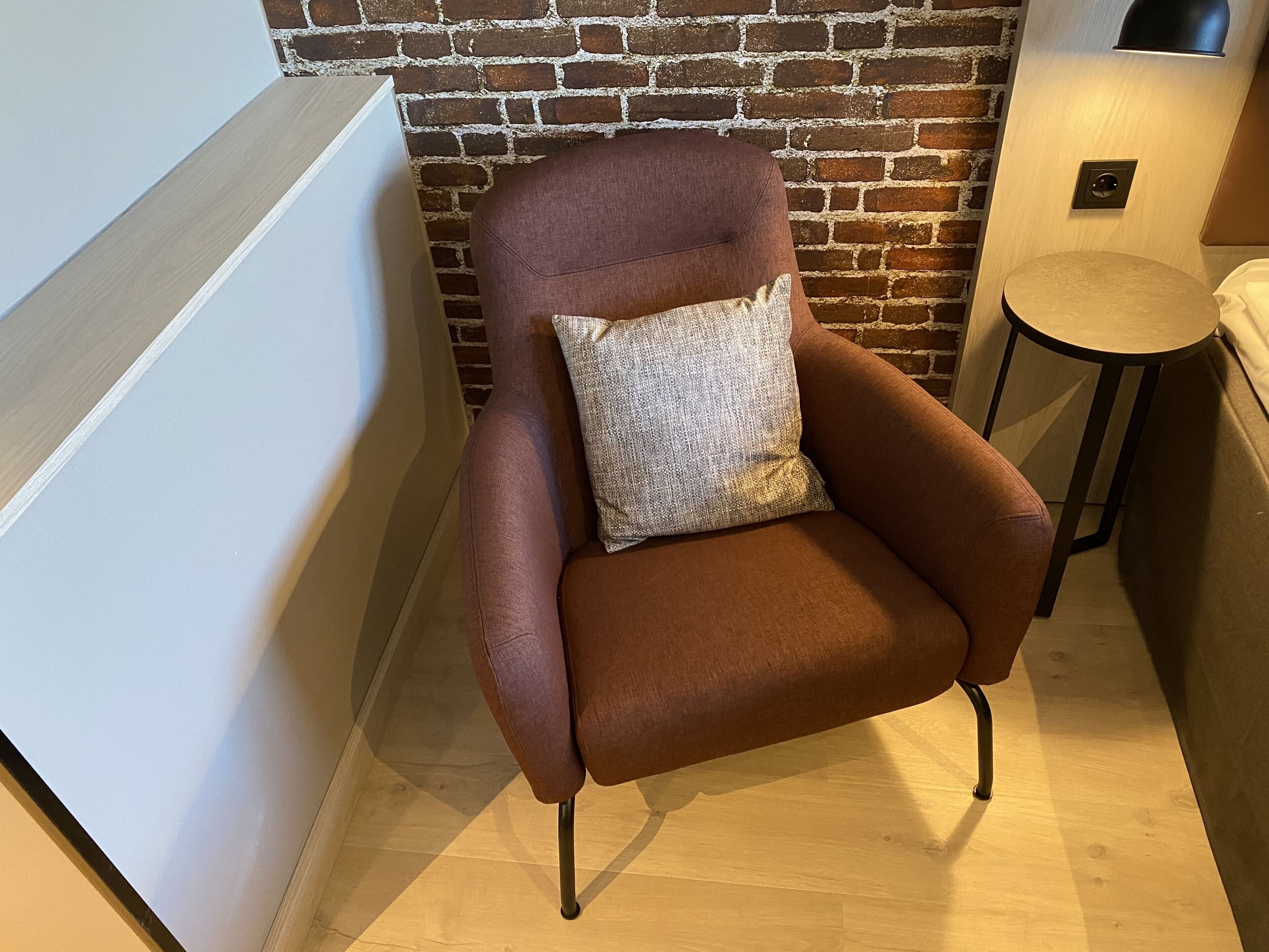 Un fauteuil marron avec un coussin à texture particulière, placé contre un mur de briques.