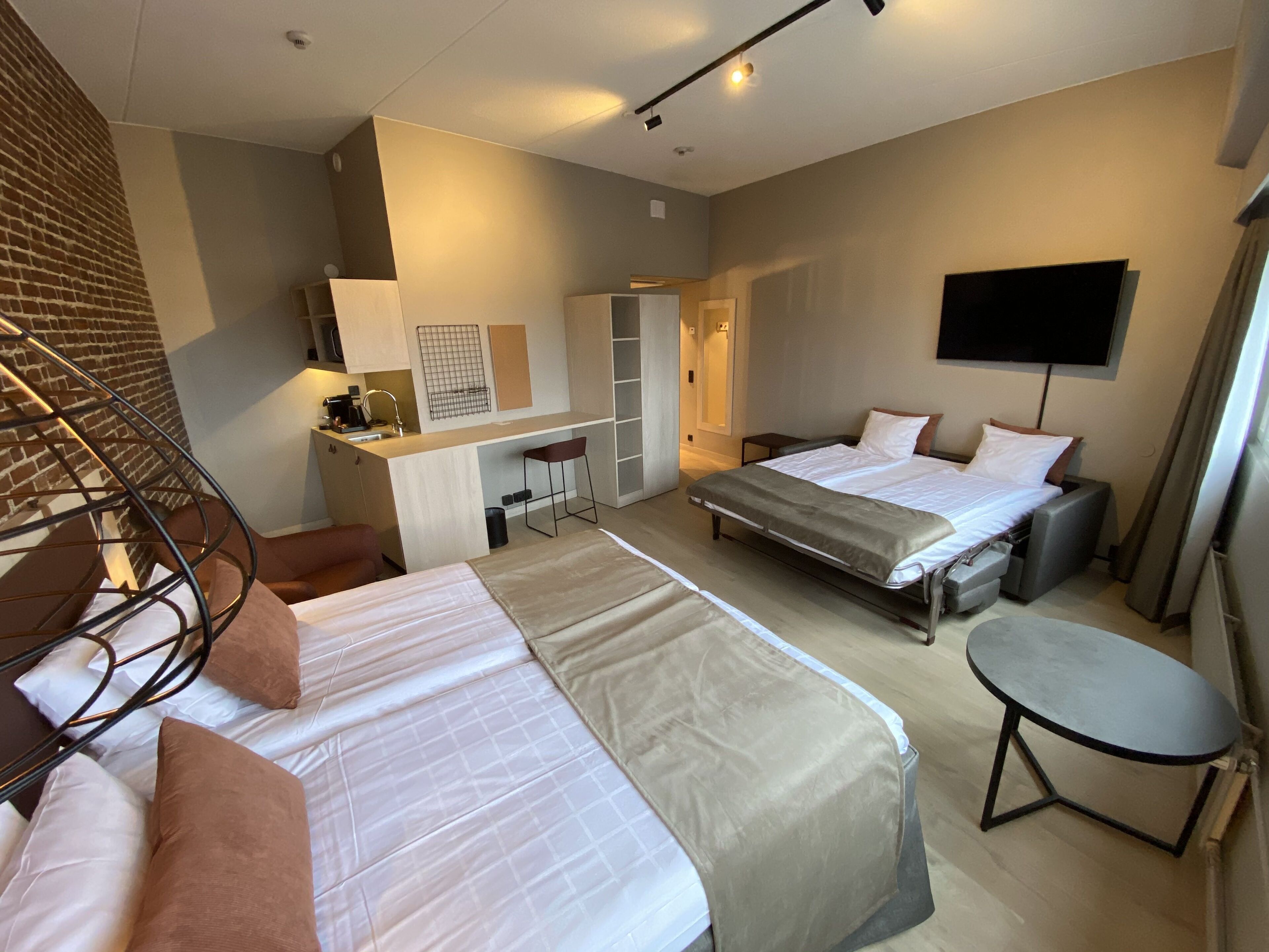 A hotel room with two beds, a desk, a chair, a TV, and a small table.
