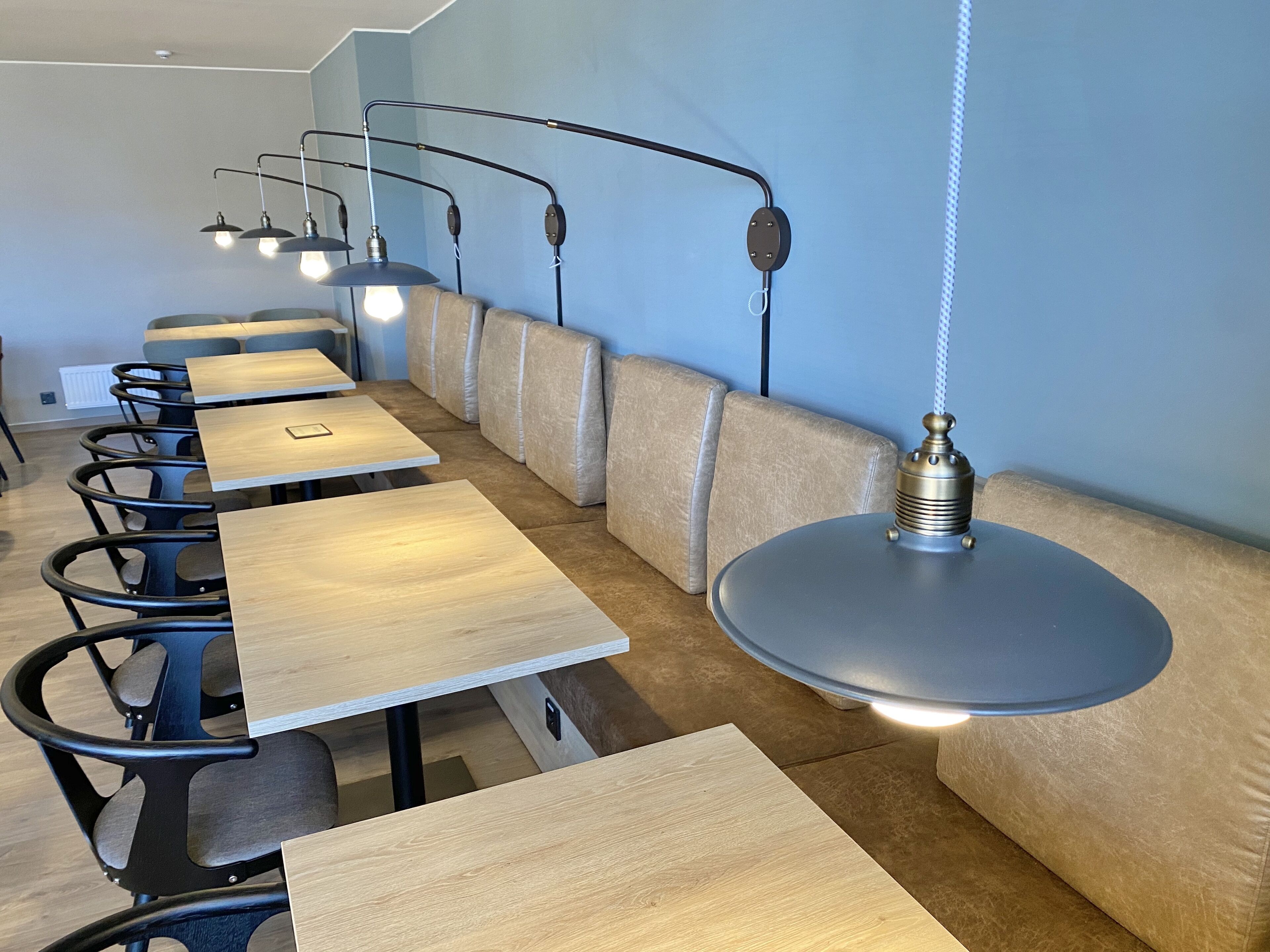 Un interior de restaurante moderno con mesas largas, bancos acolchados e iluminación colgante.