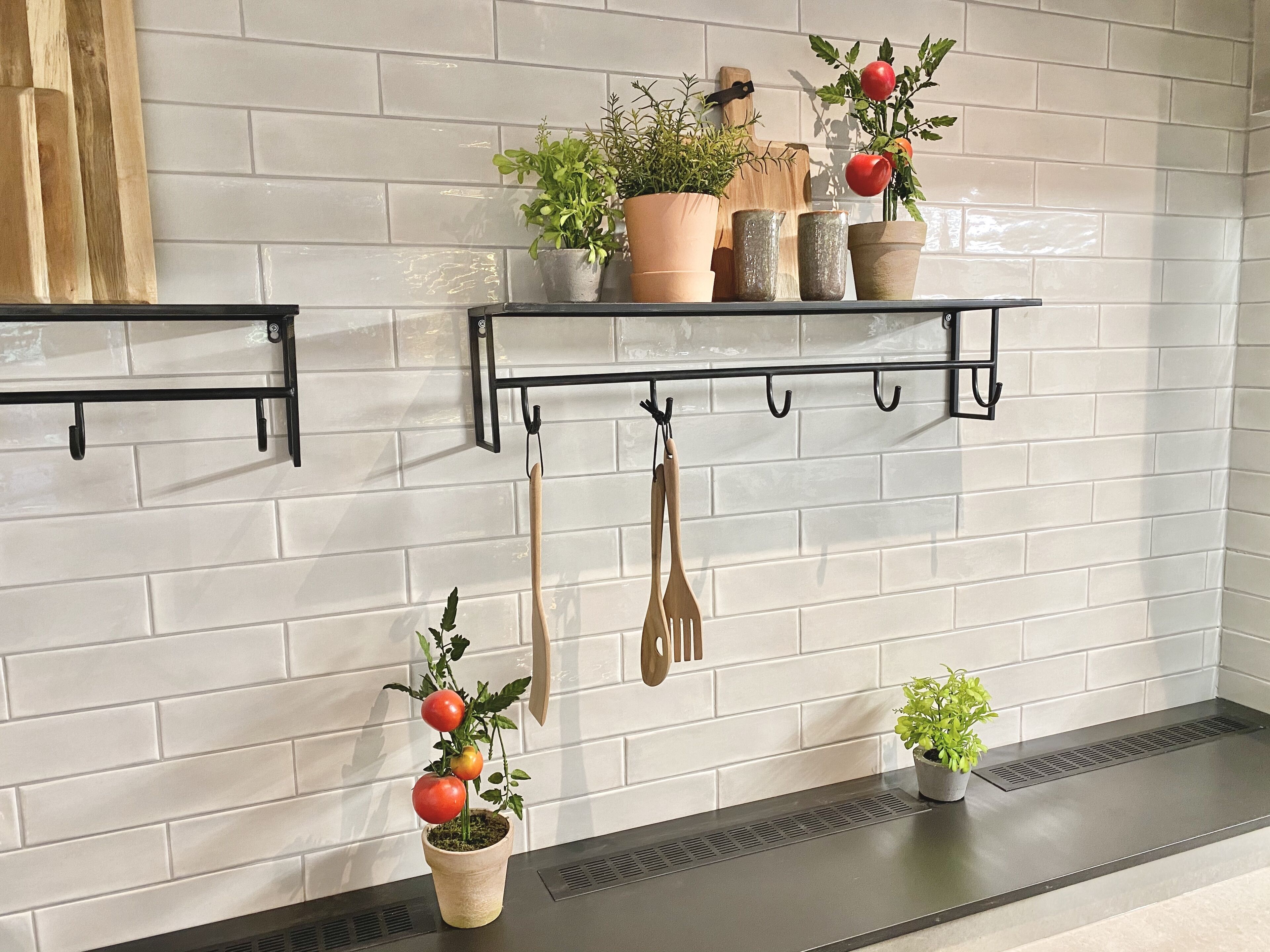 Eine Küche mit weißen Fliesenwänden, zwei schwarzen Metallregalen und mehreren Blumentöpfen.