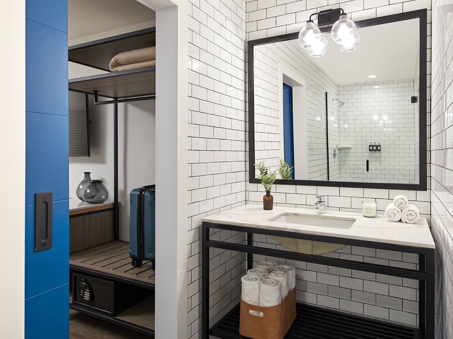 A modern bathroom with a white tiled wall, a large mirror, a sink with two bottles of shampoo, and a towel rack.