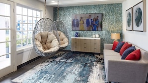 A modern living room with a hanging chair, a sofa with colorful cushions, a large flat-screen TV, and a decorative wall.