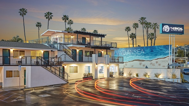 A multi-story hotel with a beach mural, palm trees, and a sign for 'Theshoal La Jolla Beach'.