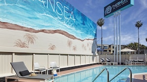 A pool area with lounge chairs, a mural of waves, and a sign for Theshoal La Jolla Beach.