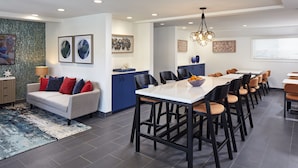A modern kitchen with a large island, dark flooring, and a dining area with high chairs.