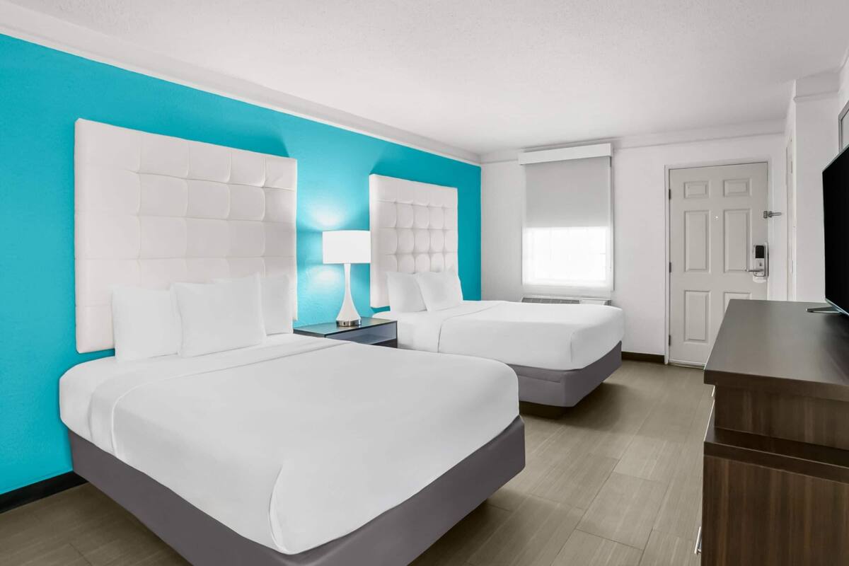 A hotel room with two beds, a desk, a TV, and a window.