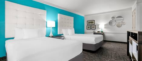 Quarto de hotel com duas camas, uma parede de destaque cor turquesa, um tapete estampado e um penteado.