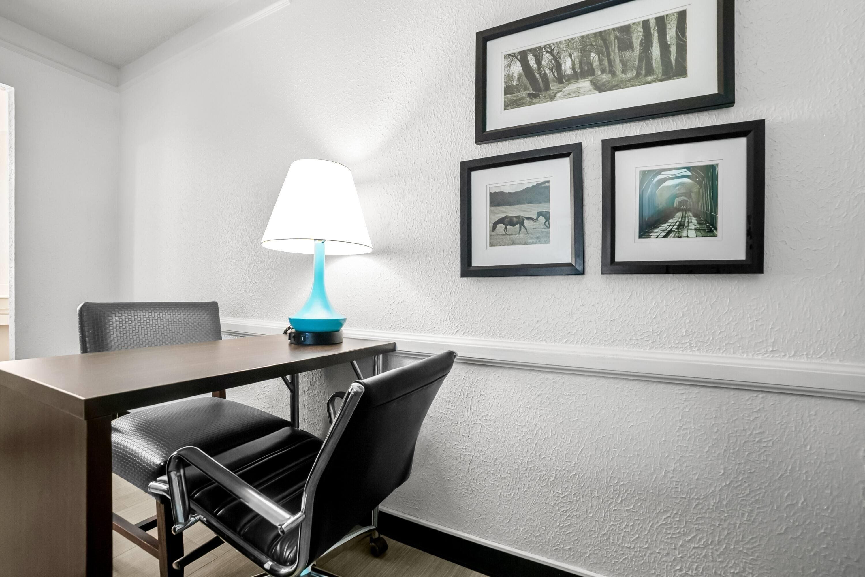 Un salón de conferencias con una mesa, sillas, una lámpara y cuadros en la pared.