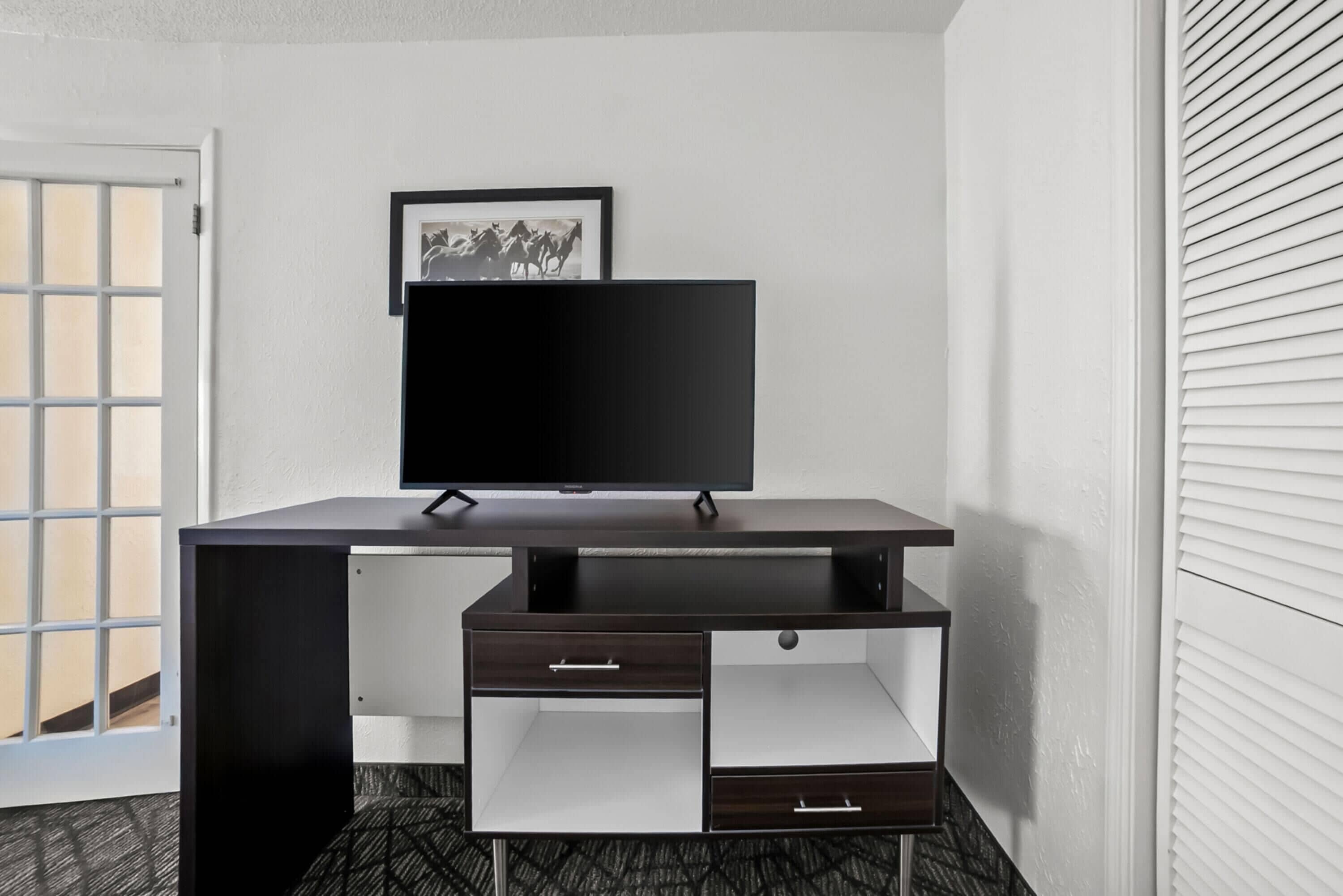 Un bureau moderne doté d’un téléviseur à écran plat, d’un tableau encadré et d’un petit meuble à tiroirs.