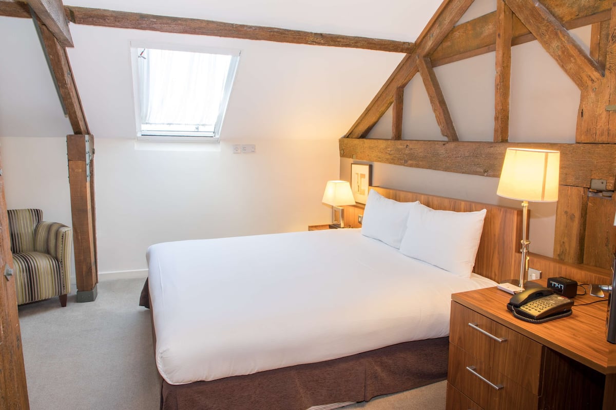 A bedroom with a large bed, wooden headboard, bedside lamps, a small desk with a telephone, and a window.