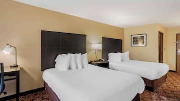 Quarto de hotel com duas camas, uma escrivaninha, uma cadeira, um abajur e um quadro na parede.