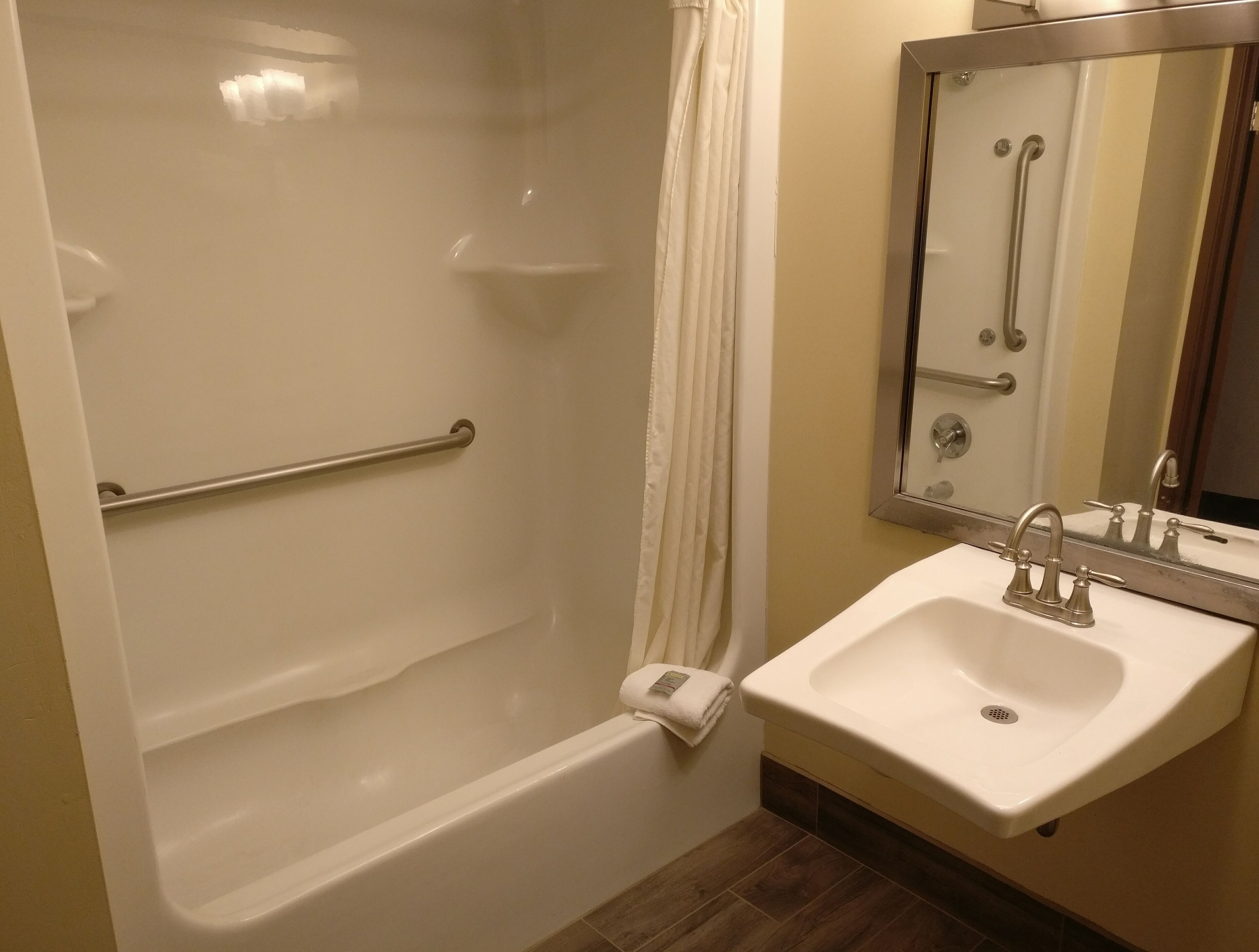 A bathroom with a bathtub, a handrail, a sink, and a mirror.
