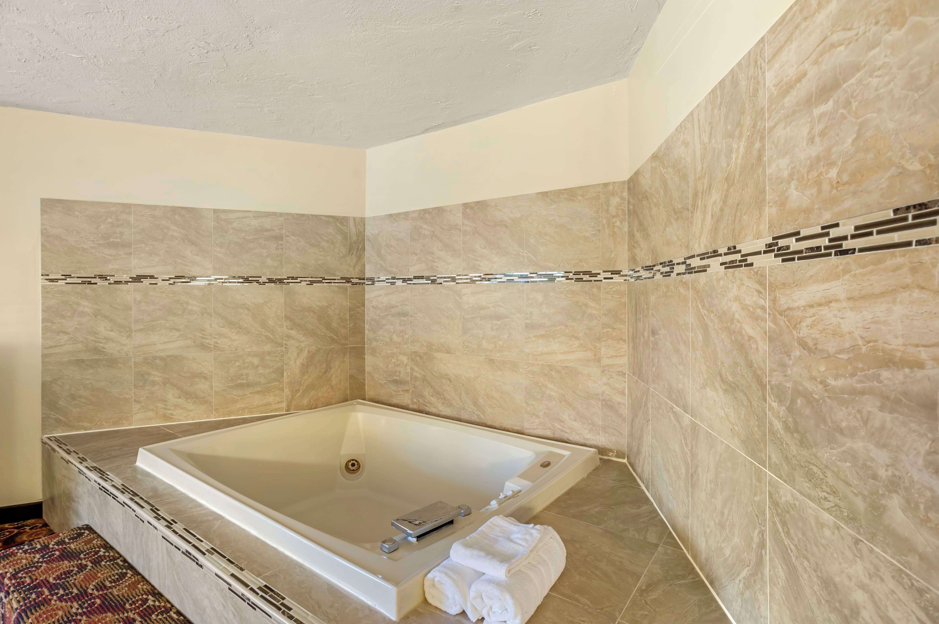 A modern bathroom with a large bathtub, beige marble walls, and a decorative tile border.