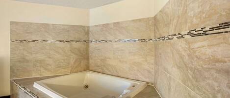 Une salle de bain moderne avec une grande baignoire, des murs en marbre beige et une bordure décorative en carreaux.