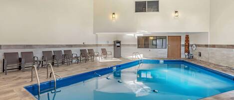 Una piscina interior amplia con muelle de madera y sillas de descanso.