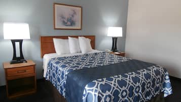 Habitación de hotel con cama, dos mesitas de noche con lámparas, una mesita de noche con cajón, un cuadro en la pared y suelo alfombrado.
