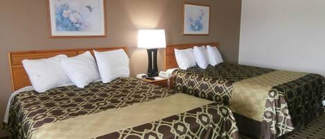 Habitación de hotel con dos camas, cada una con cubrecamas estampados, una mesita de noche con lámpara y dos cuadros enmarcados con motivos florales en la pared.