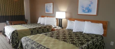 A hotel room with two beds, a desk, a chair, a lamp, and two framed pictures on the wall.