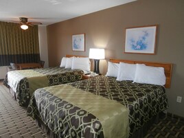 A hotel room with two beds, a desk, a chair, a lamp, and two framed pictures on the wall.