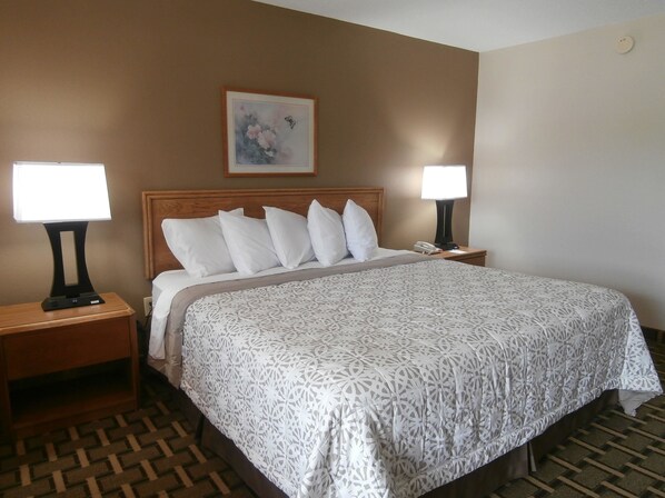 A hotel room with a large bed, two bedside tables, a nightstand, a wall-mounted telephone, and a framed picture above the bed.