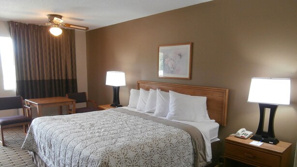 A hotel room with a large bed, two bedside tables with lamps, a desk, and a chair. - Americas Best Value Inn Blue Ridge (Blue Ridge)