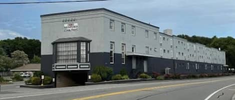 A large, multi-story hotel building with a sign reading "Bedford Plaza Hotel." The building has a modern architectural style with a flat roof and a mix of rectangular and square windows. There are no visible amenities or features indicating the hotel's interior or specific services.