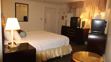 A hotel room with a bed, bedside table, lamp, dresser, mirror, and a small round table.