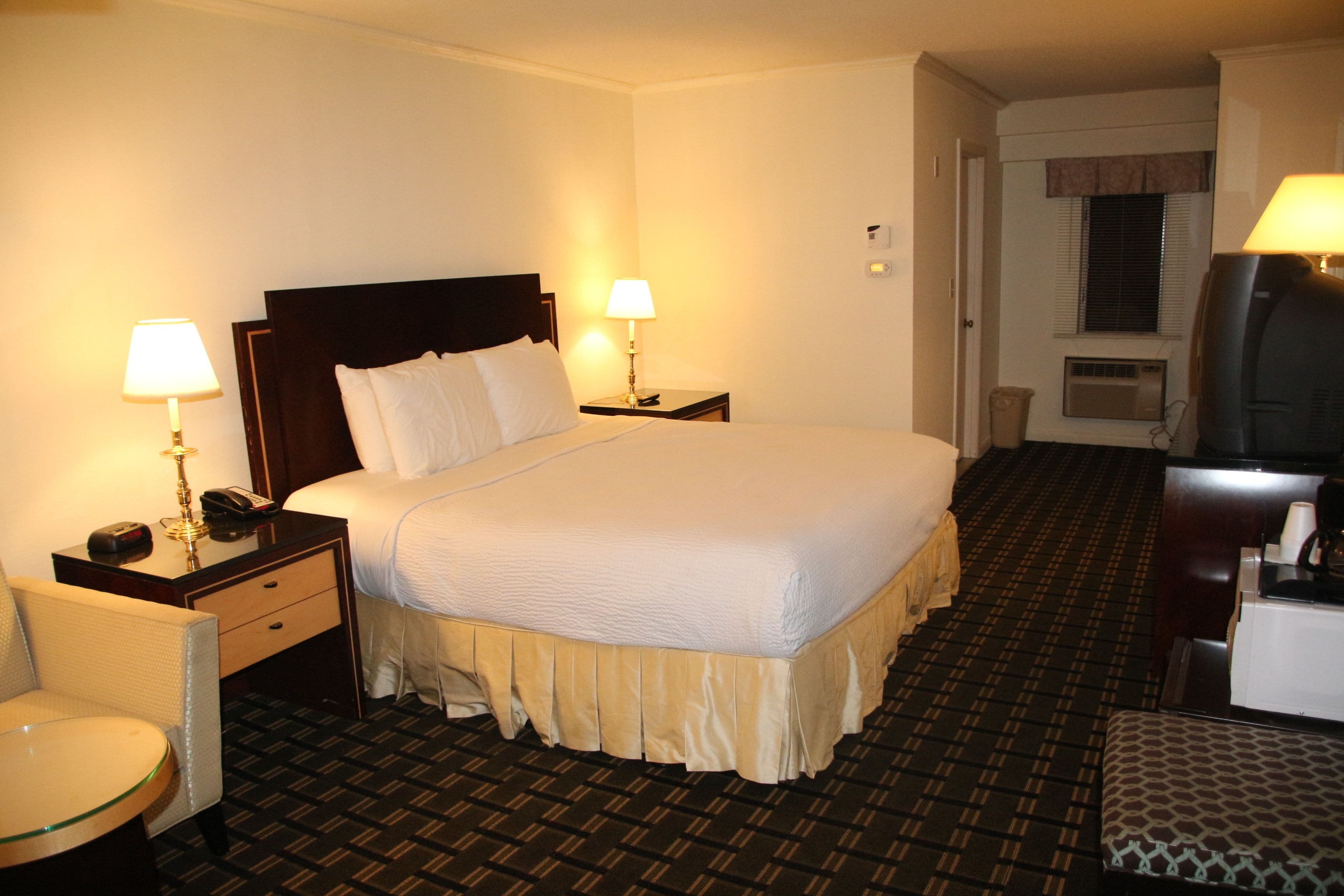 A hotel room with a large bed, two bedside tables with lamps, a chair, and a television.