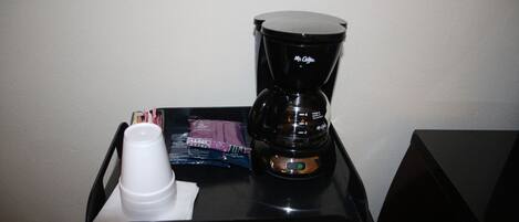 Una bandeja negra con una cafetera, una taza blanca y un paquete de pañuelos.