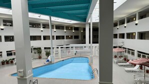 Una piscina interior de varios niveles con agua azul, paredes blancas y un techo con vigas azules.