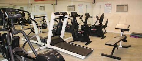 Un gimnasio con cintas de correr, elípticas y una banca.