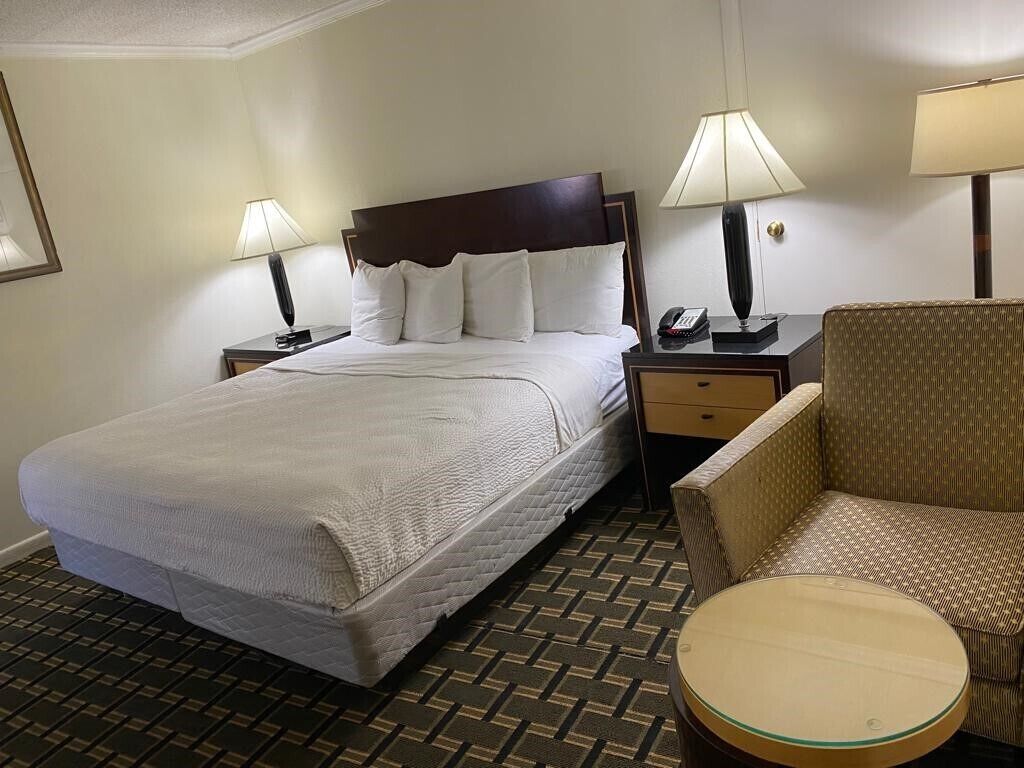 A hotel room with a bed, two bedside tables with lamps, a chair, and a small table.