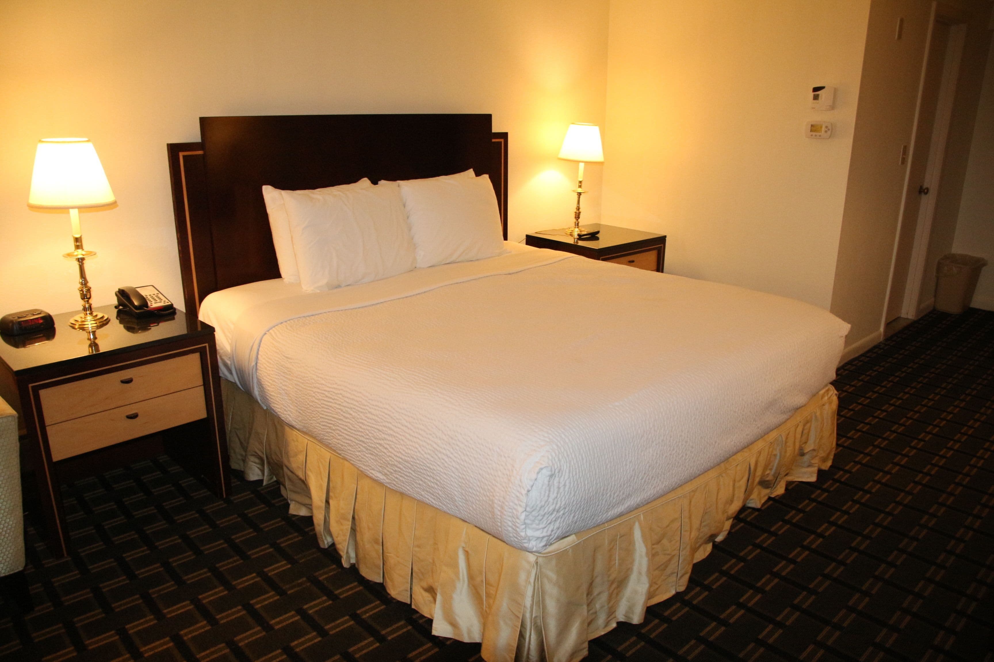 A hotel room with a large bed, two bedside tables with lamps, a telephone, and a waste bin.