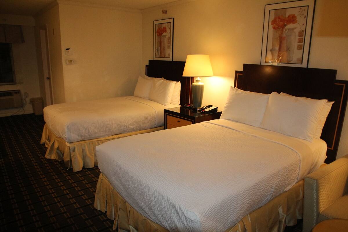 Ein Hotelzimmer mit zwei Betten, einem Nachttisch mit Lampe und einem gerahmten Bild an der Wand.