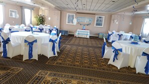 Un salón de banquetes con mesas redondas, manteles blancos y cintas azules.