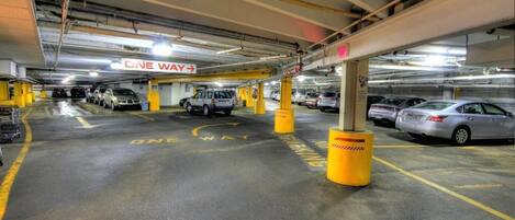 Un estacionamiento con varios niveles, carriles de circulación de sentido único bien señalizados y pilares de protección amarillos.
