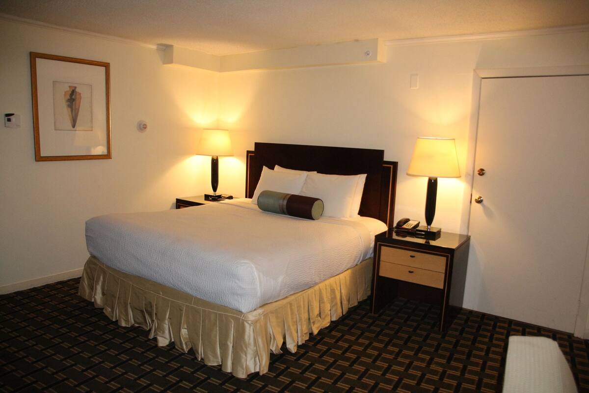 Ein Hotelzimmer mit einem großen Bett, zwei Nachttischen mit Lampen, einem gerahmten Bild an der Wand und einer Tür.