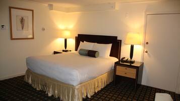 Habitación de hotel con una cama grande, dos mesitas de noche con lámparas, un cuadro enmarcado en la pared y una puerta.
