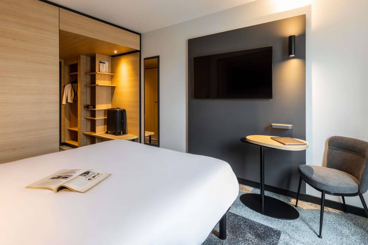 Une chambre d’hôtel moderne équipée d’un lit, d’un bureau, d’une chaise, d’une télévision et d’une armoire.