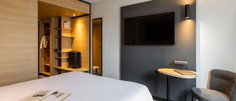 Una habitación de hotel moderna con cama, escritorio, silla, televisor y armario.