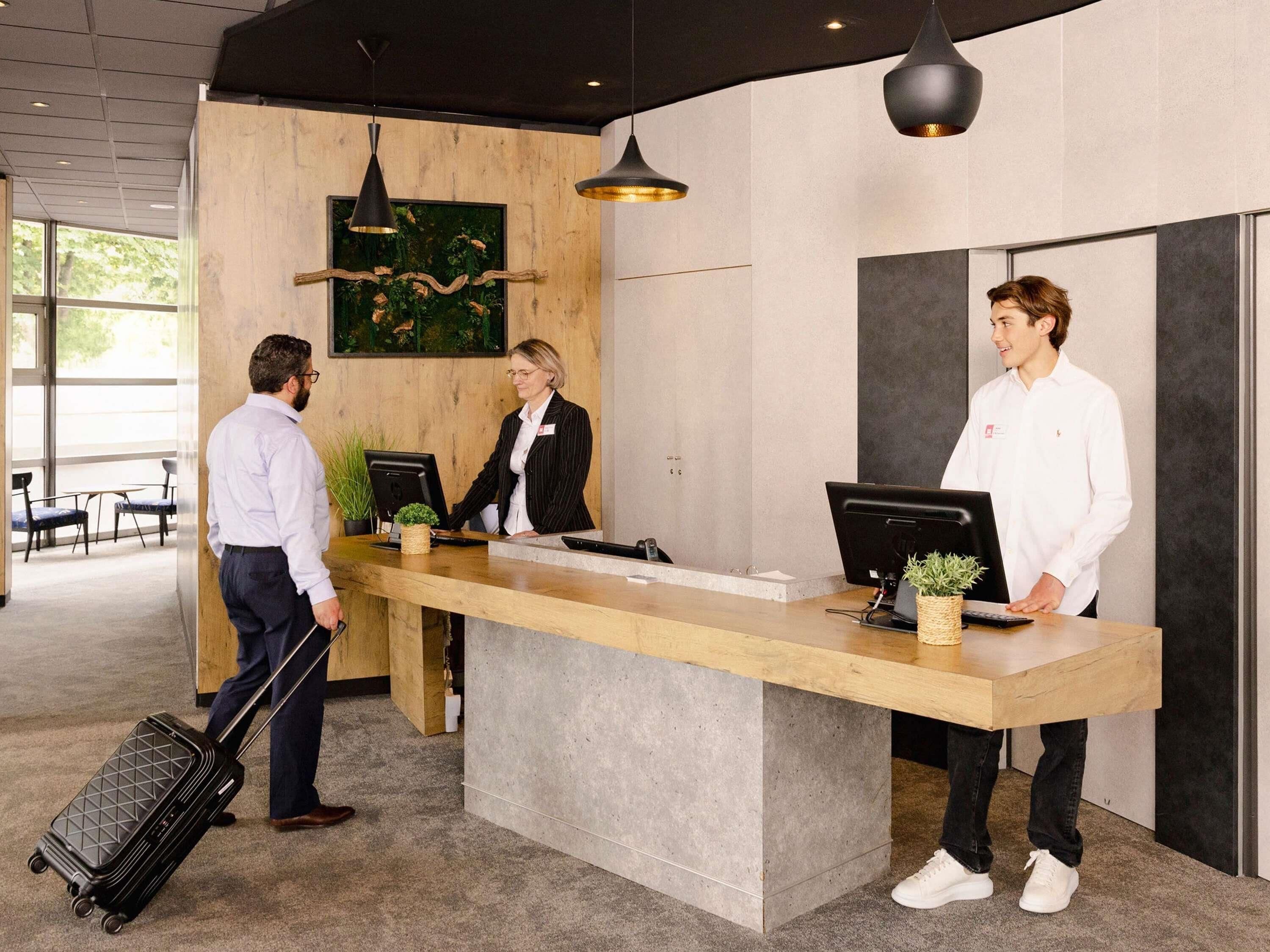 A reception desk with two monitors, a wooden counter, and a large window with a view of greenery.