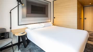Une chambre d’hôtel moderne, dotée d’un grand lit, d’un bureau avec une chaise, d’une œuvre d’art encadrée au mur et d’une armoire.