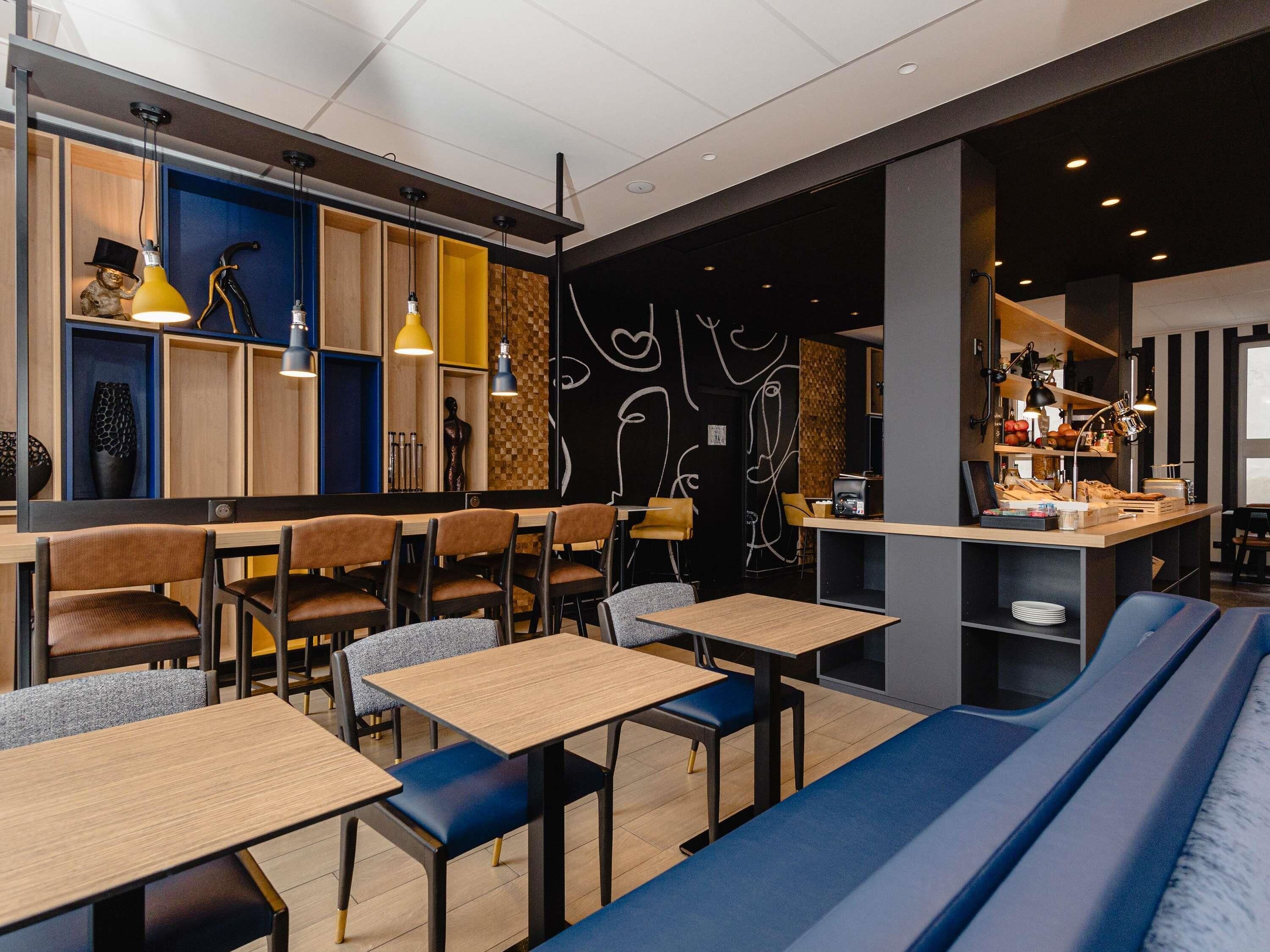 A modern cafe with wooden tables, blue cushioned seating, and a black wall with white abstract art.