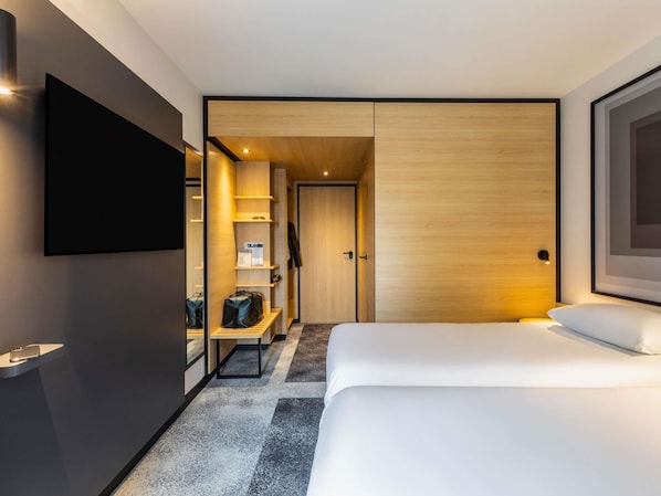 Una habitación de hotel moderna con una cama grande, un televisor de pantalla plana en la pared, un armario de madera y un pequeño espacio de descanso con una mesa y sillas.