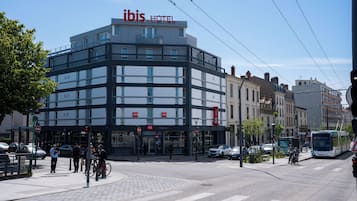 Un hôtel moderne, reconnaissable à son grand panneau « IBIS HOTEL », situé près d’un passage piéton et d’une ligne de tramway.
