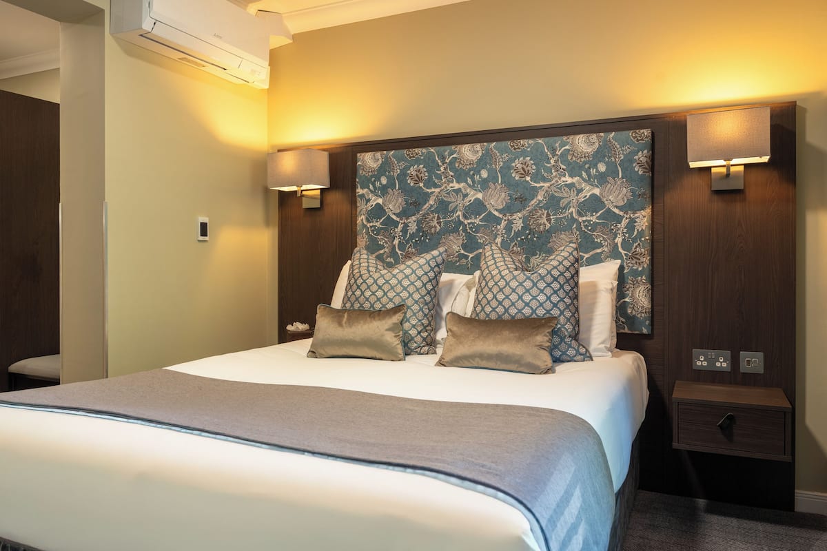 A hotel room with a large bed, a headboard with a floral pattern, bedside lamps, and a small nightstand.